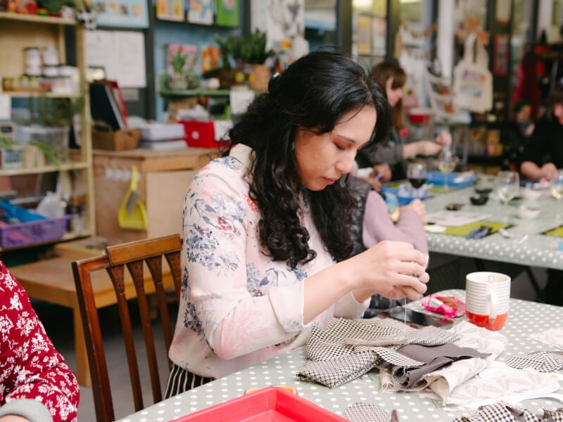Woman surrounded by fabric, concentrating on sewing something