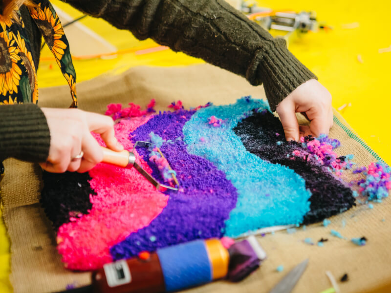 Woman using a tool to shave a colourful tufted rug