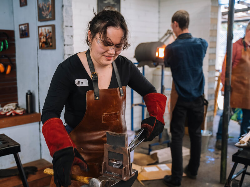 A person tries blacksmithing at an anvil