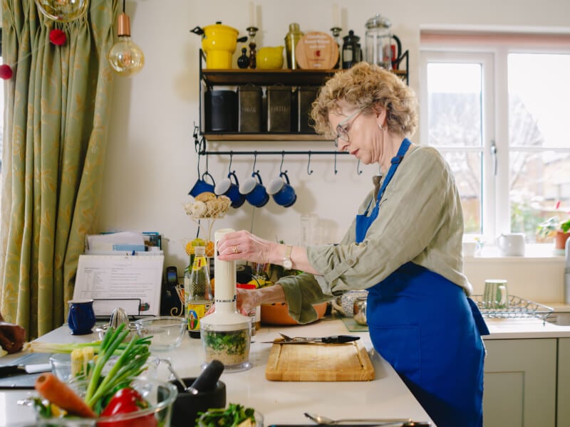 Women in blue apron in a kitchen, blending ingredients