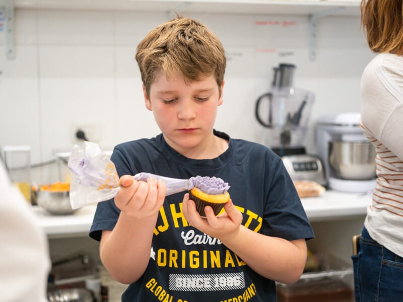 Young boy icing a cupcake with purple buttercream