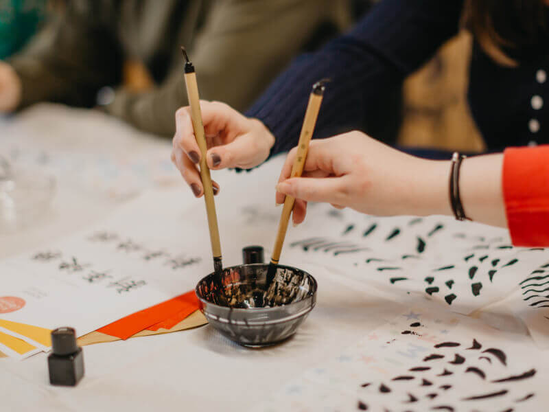 A couple both dip their calligraphy pens into an ink pot