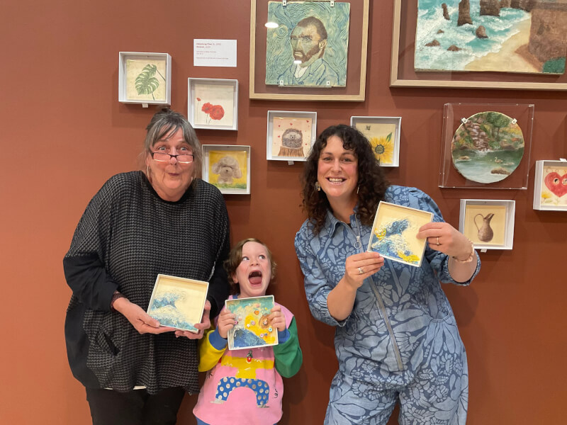 A family of three pose with their finished chocolate paintings