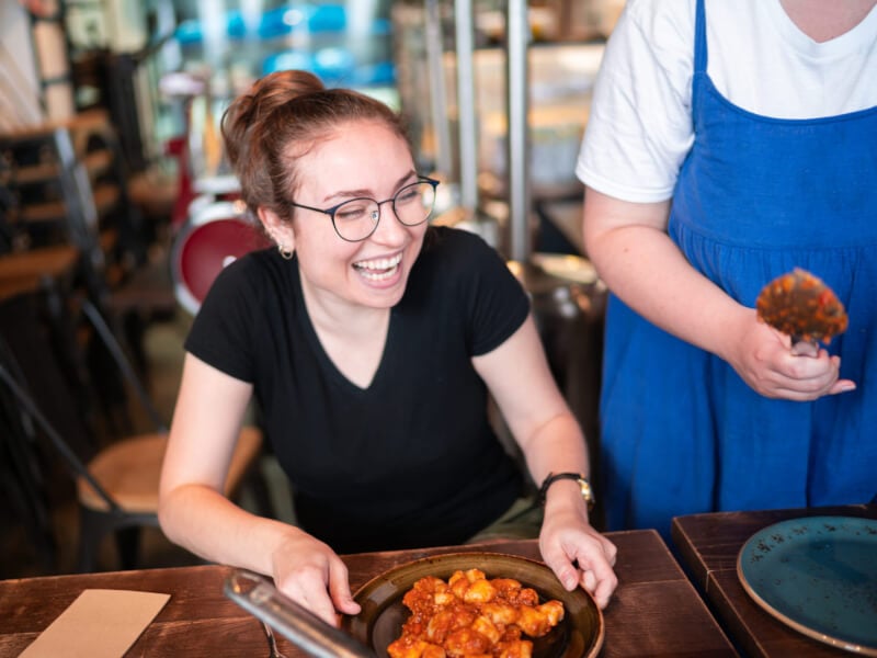 A woman is smiling as she holds a plate of tomato pasta 
