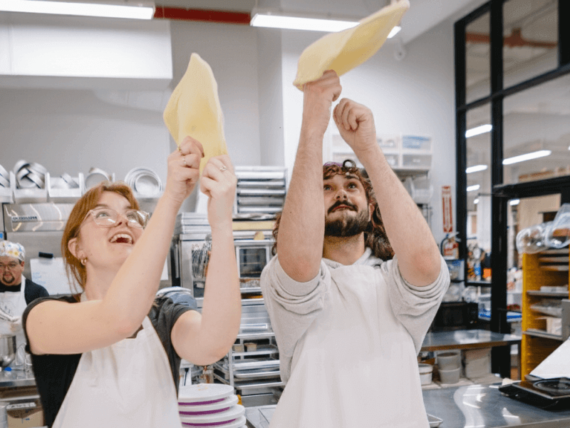 A couple laugh while throwing pizza into the air at cooking class