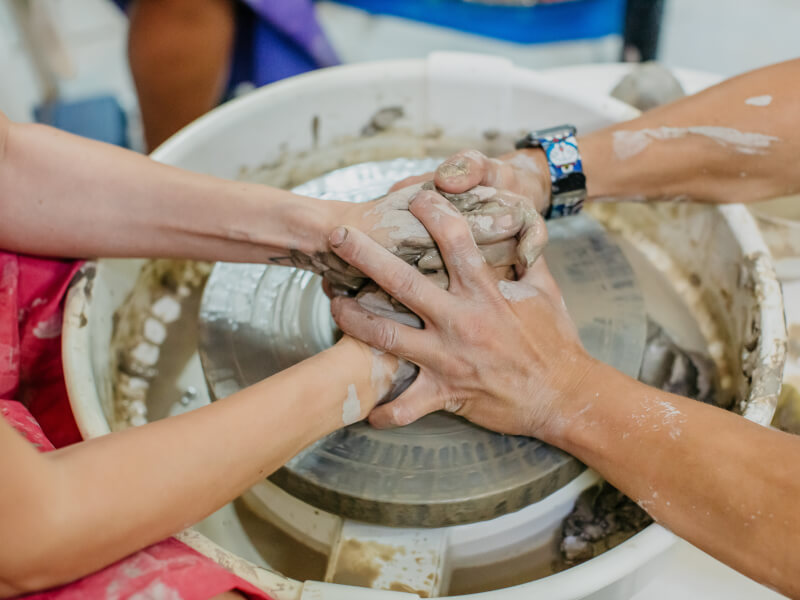 Two sets of hands touching over wheel thrown clay
