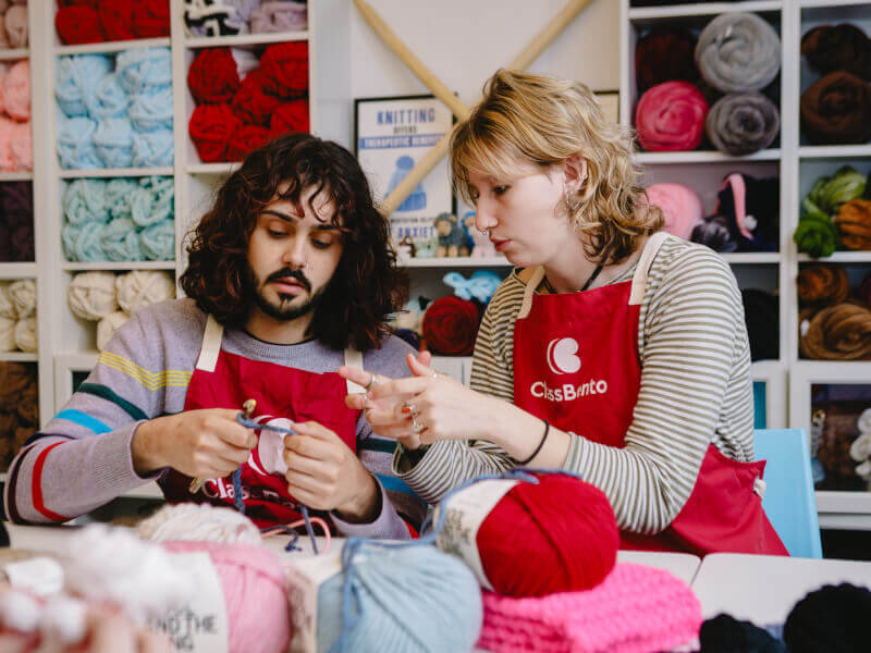 A couple at a crochet class surrounded by yarn