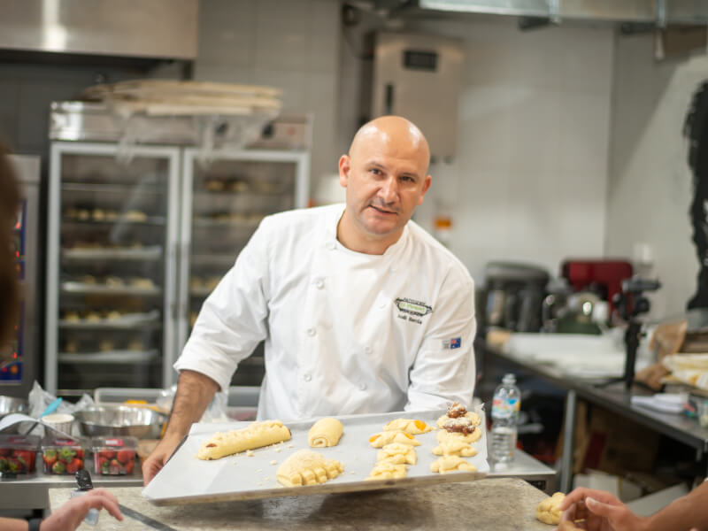 Man holding a tray of freshly made croissants ready for oven
