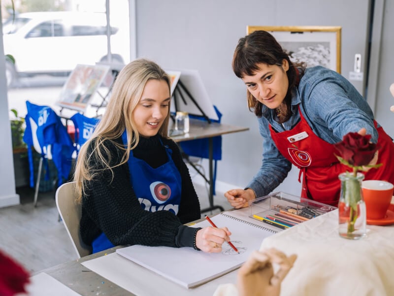 A woman practices drawing a rose with the help of a drawing teacher