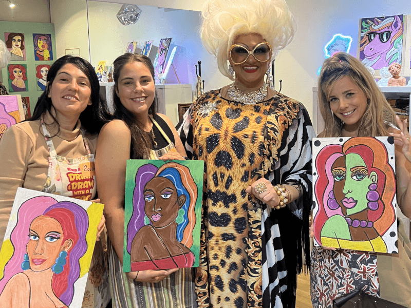 Three friends pose with a drag queen and their drawings