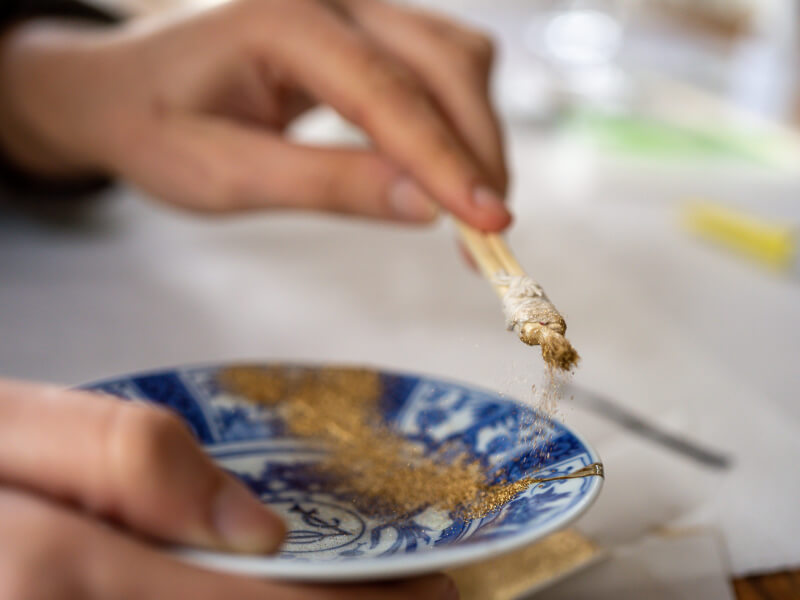 Hand applying gold lacquer to broken plate in the style of Kintsugi