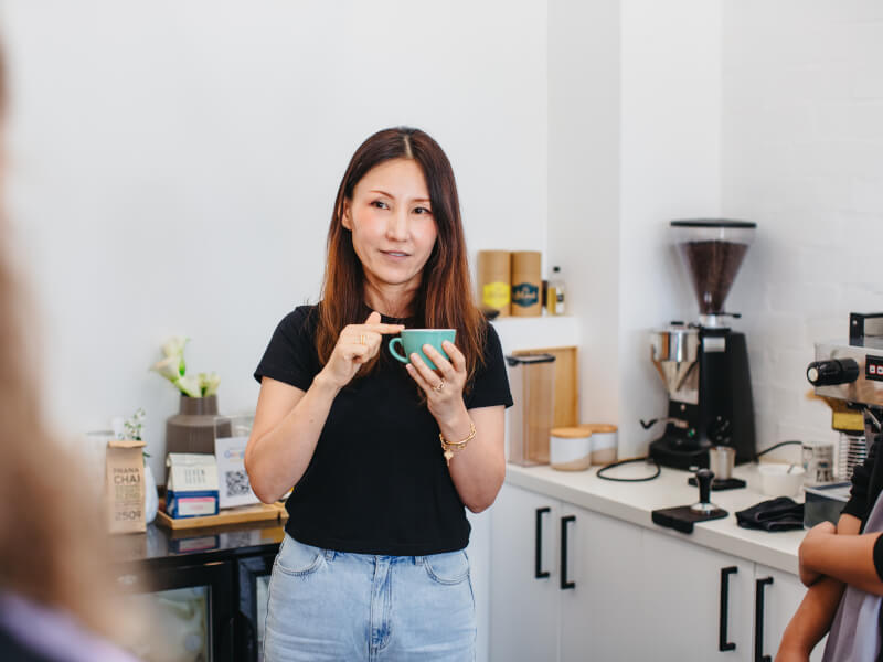 A woman holding a cup of coffee and explaining coffee concepts to group of students