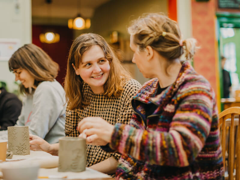 Two friends chat while they make coffee mugs