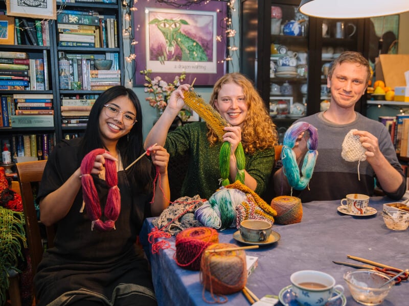 Three friends at a crochet class holding colourful yarn