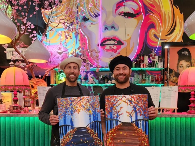Two friends show off their finished painting in a vibrant art studio
