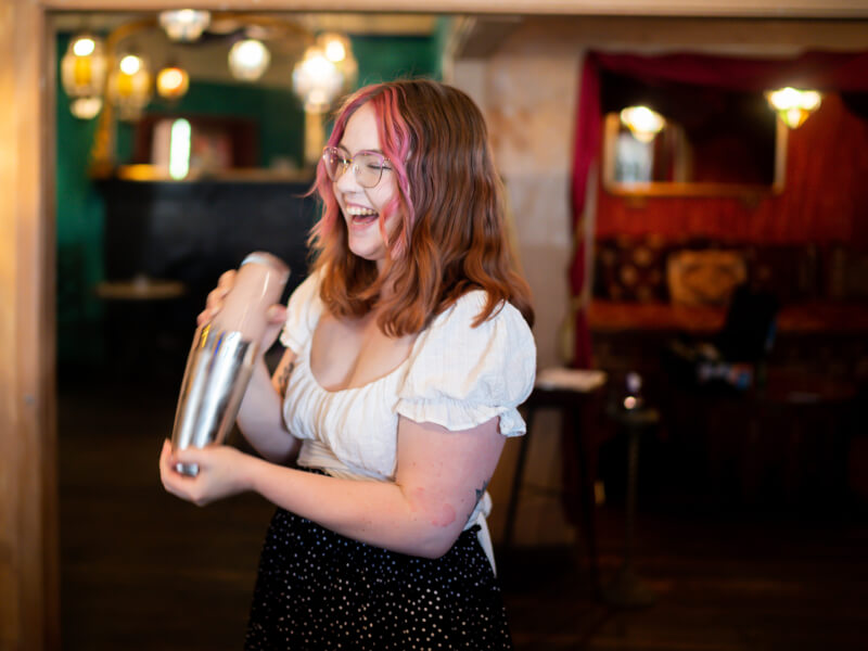 A woman smiles while shaking a cocktail at a cocktail class