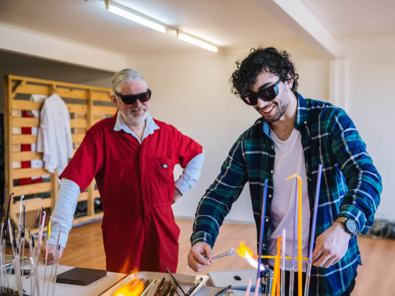 A man melts glass rods at glassblowing class he was gifted