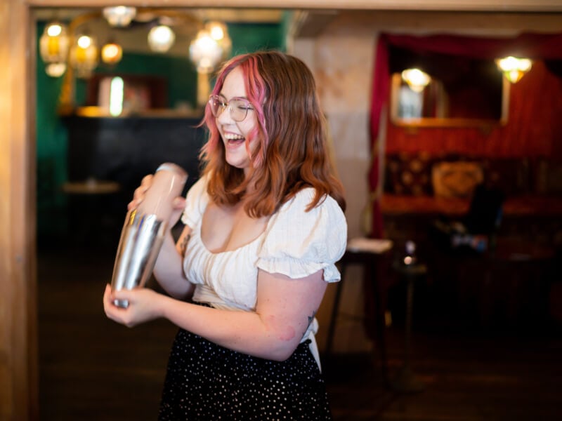 A woman laughing as she shakes a cocktail