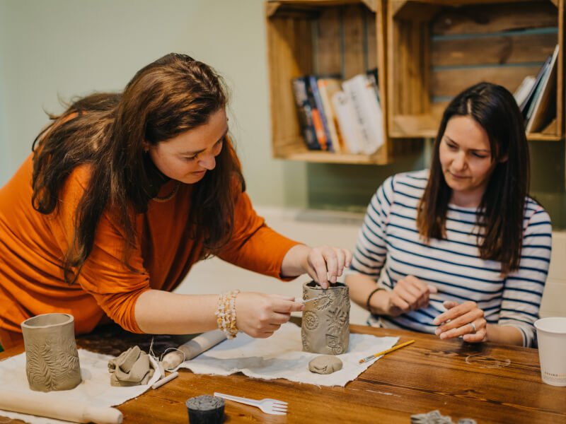 Two women helping each other at a Mothers Day pottery class