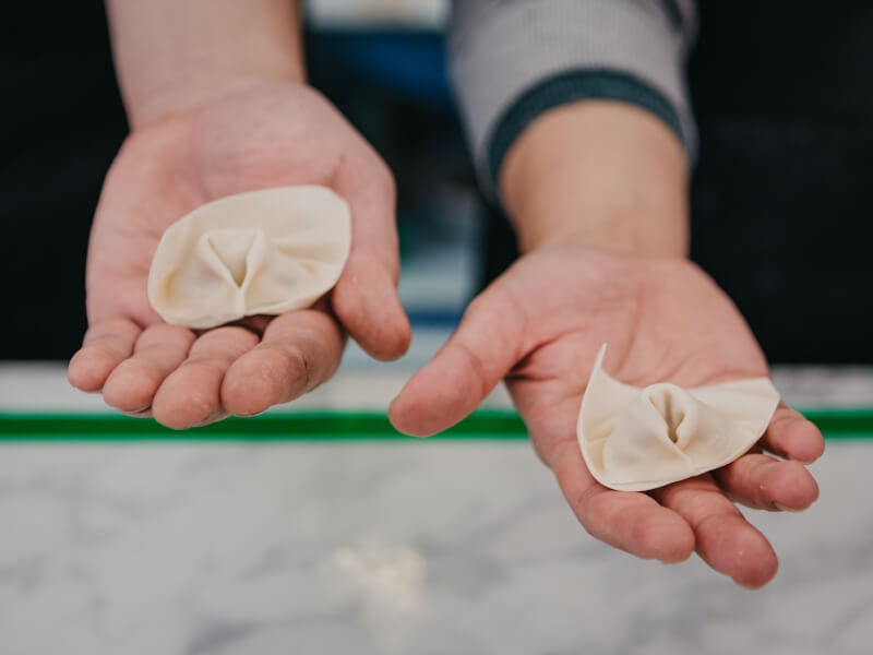 Two hands holding handmade dumplings at Brisbane cooking class