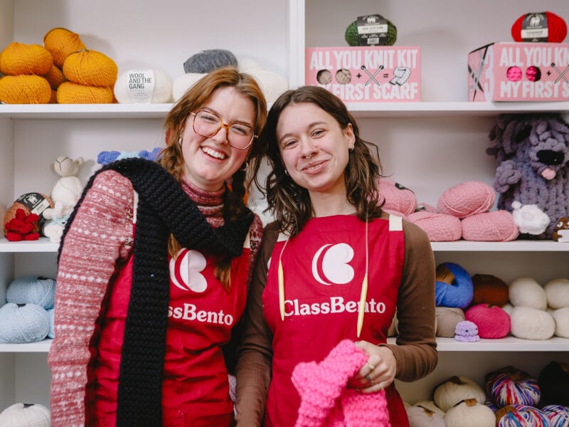 Two friends in ClassBento aprons smiling with fresh knitted scarves