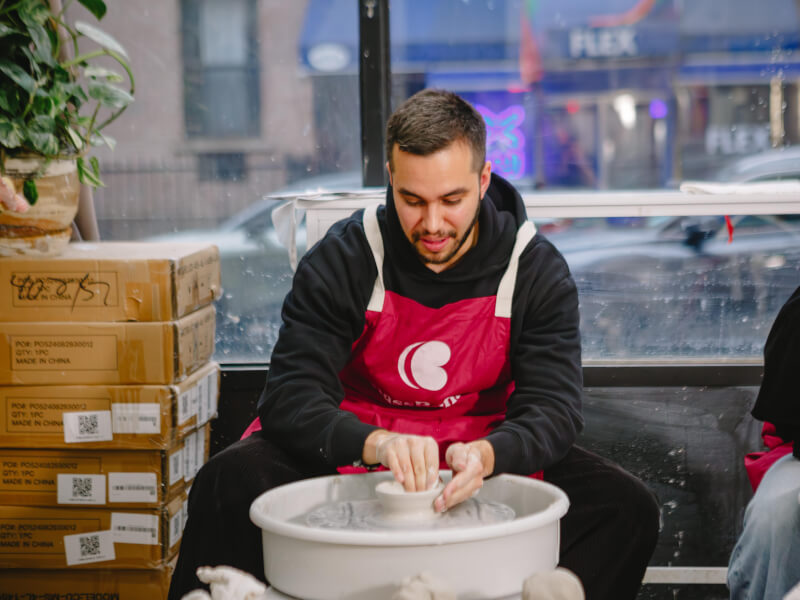 A man in a ClassBento apron learning to use the potter's wheel at a pottery class