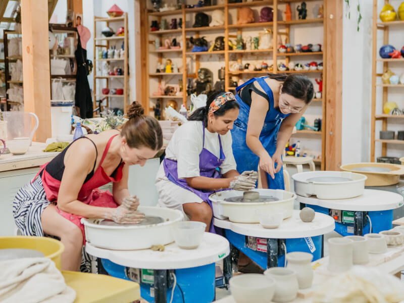 A pottery teacher helping students with wheel throwing
