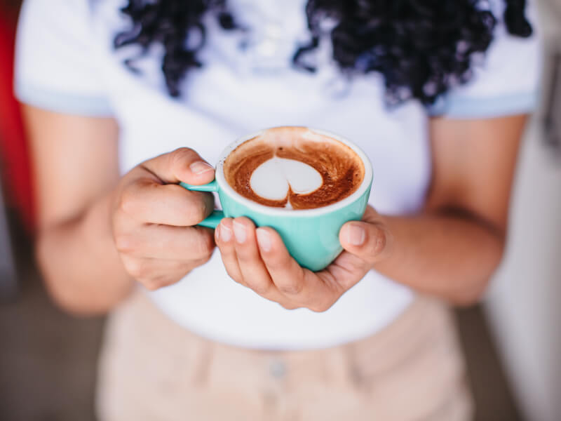 A girl holds a cup of coffee with heart shaped latte art