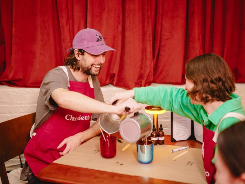 A couple pouring wax into each others candle containers