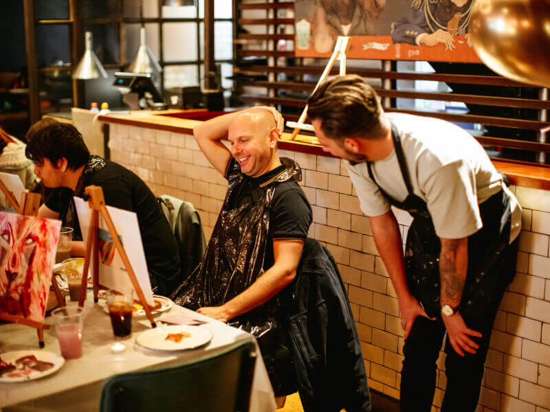 Man and art teacher laughing at brush and drink class in Sydney