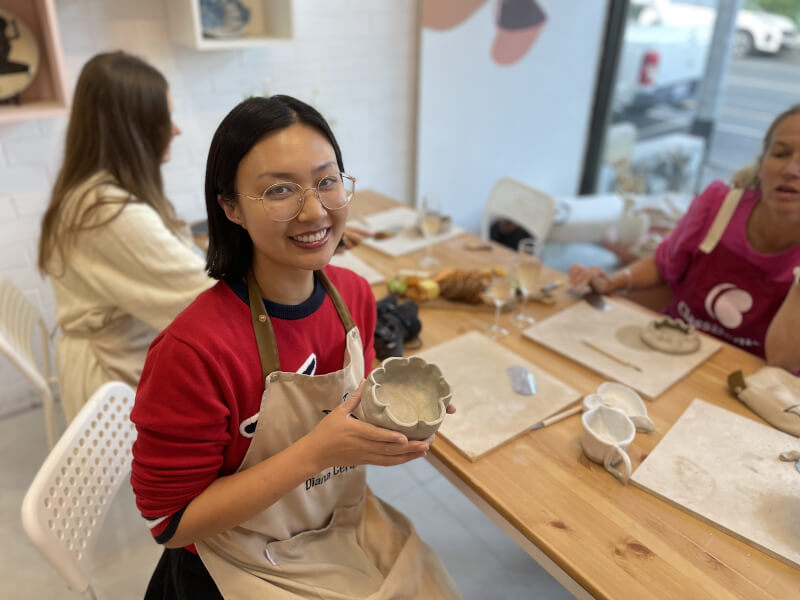A pottery student holding her handmade mug and smiling