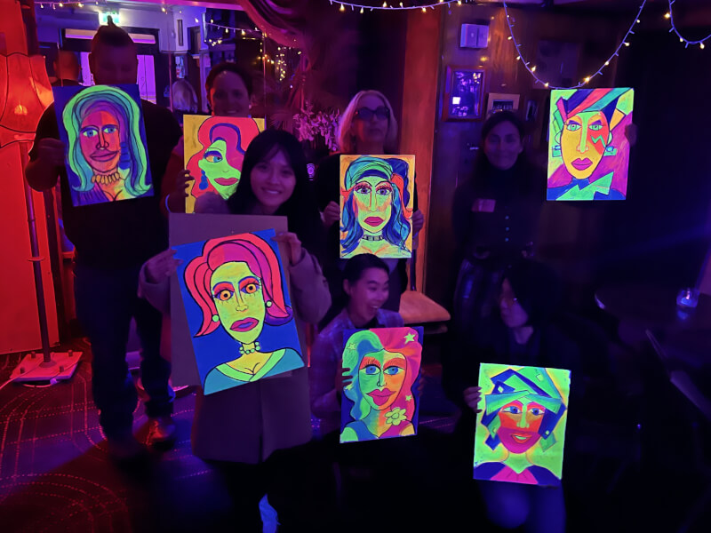 A fun group poses with their neon drawings at a drink and draw workshop