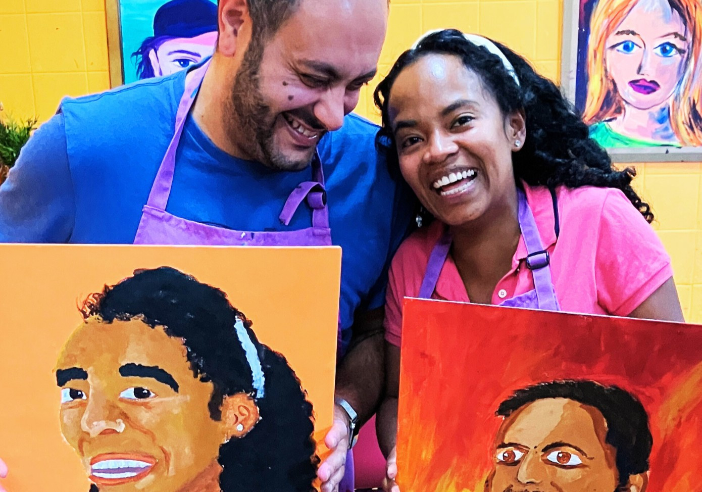 A couple laughing and holding paintings of each other