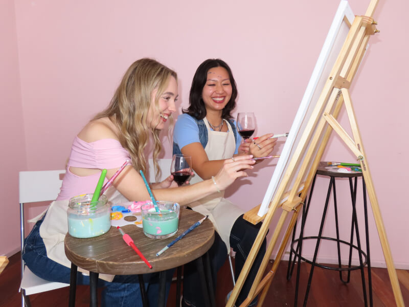 Two girlfriends sip wine and paint to celebrate galentines day