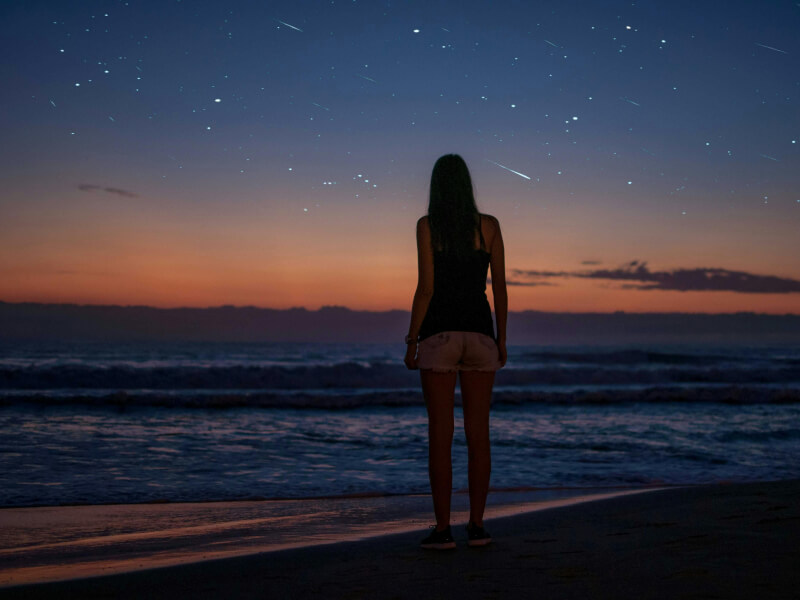 Girl standing on beach at night staring at the stars