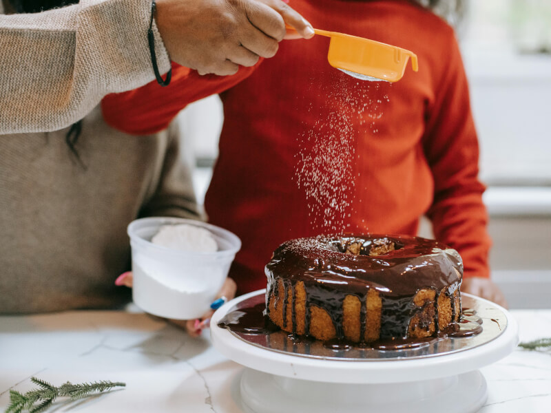 Person dusting a chocolate bunt cake with icing