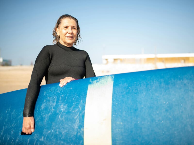Mature-age woman in a wetsuit holding a longboard