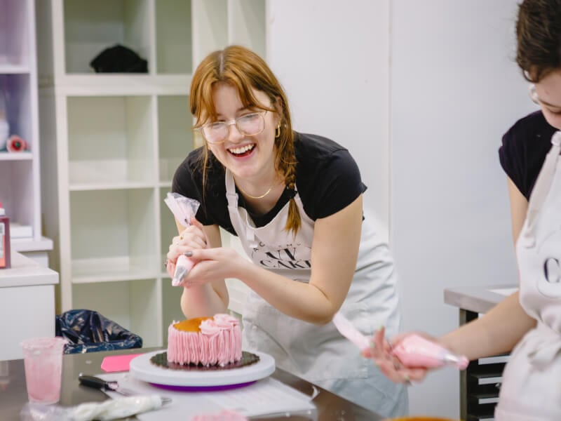 A girl smiling while she decorates a cake with pink frosting