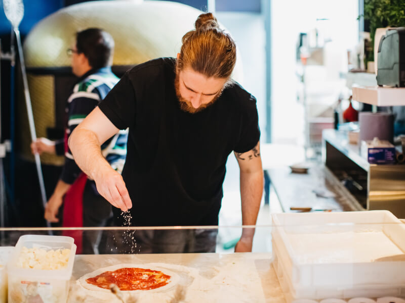 Man sprinkling cheese over homemade pizza base at pizza making class