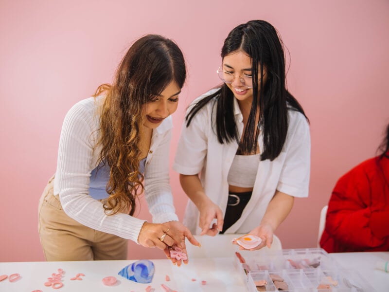 Two friends making polymer clay earrings in a cute pink workshop