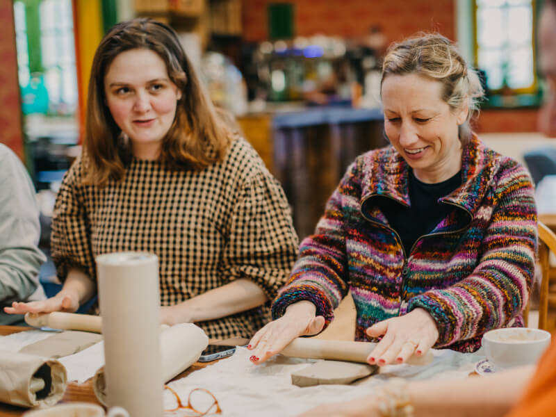 Women rolling out clay at a pottery class they were gifted for Mother's Day