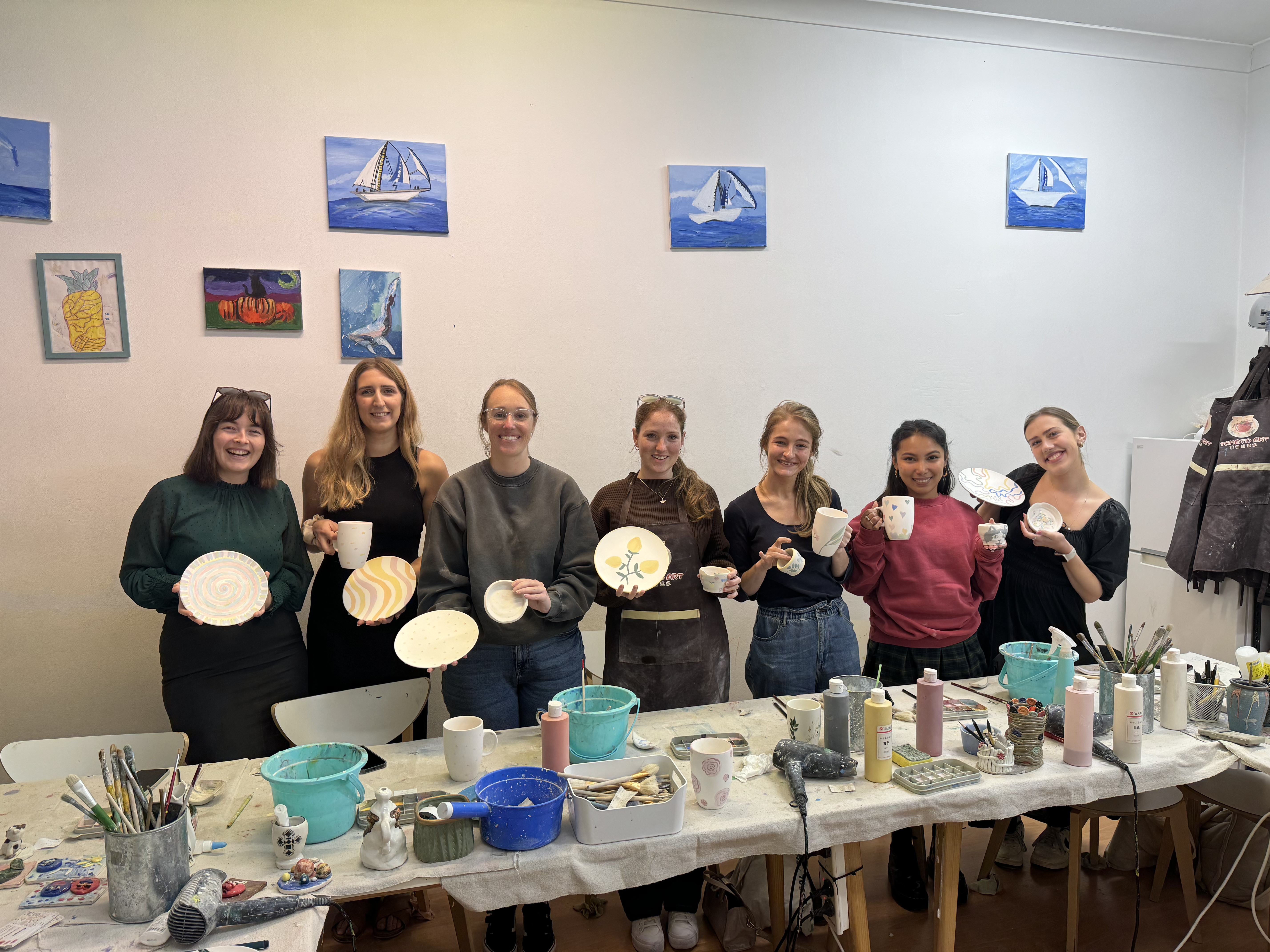Women showing off their handmade painted pottery pieces