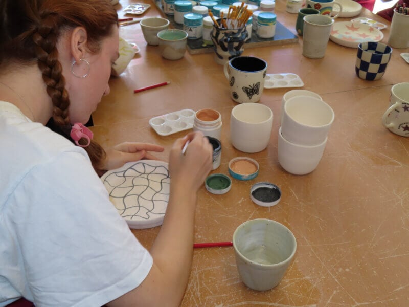 A woman paints pottery from a craft kit