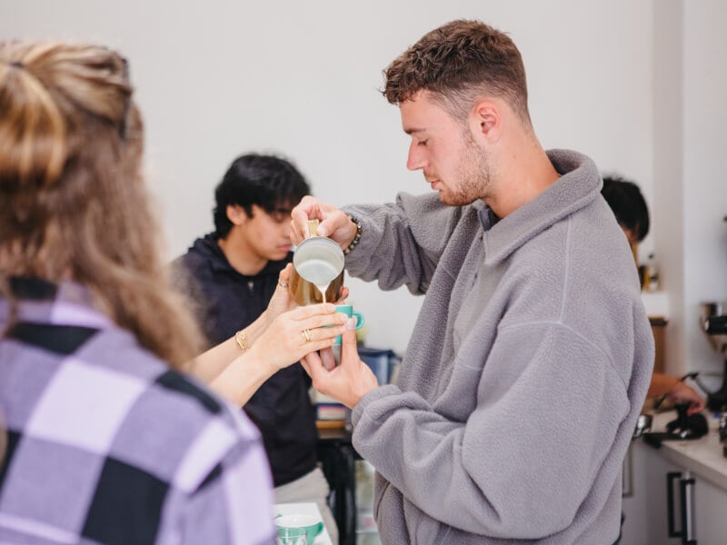 A man pours milk into his coffee cup at latte art class he was gifted
