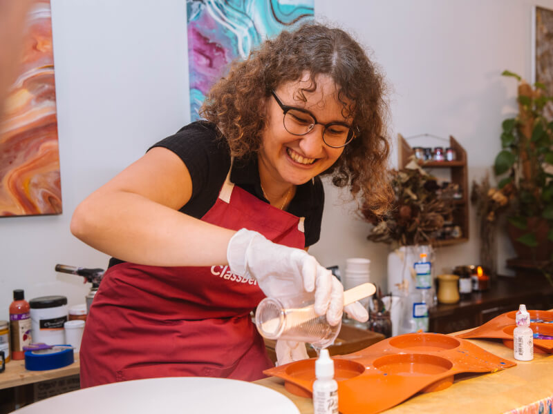 A woman smiles while pouring paint at abstract art class