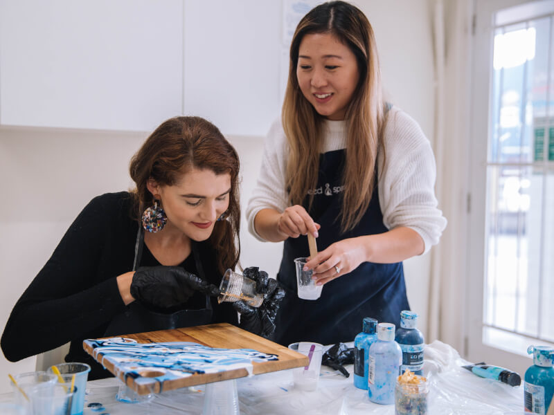 Two women with half finished resin art cheese board