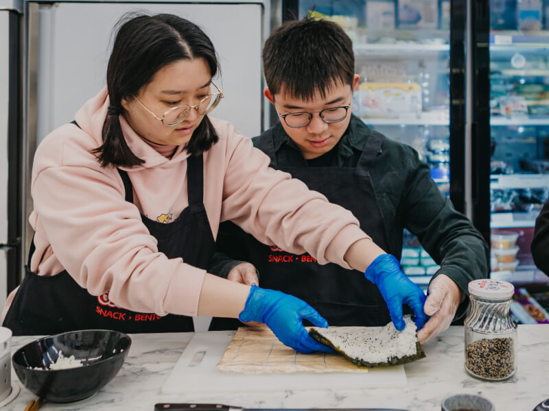man and woman rolling sushi in a cooking class