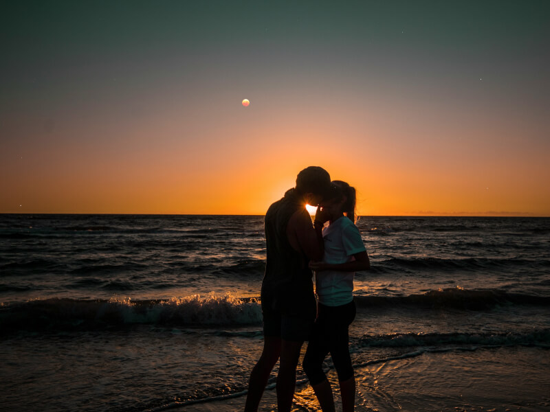 A couple share a kiss while the sun rises in the background