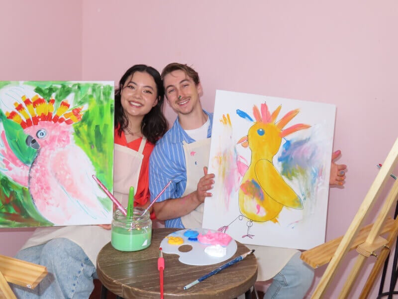 A couple show their finished artworks at a paint and sip