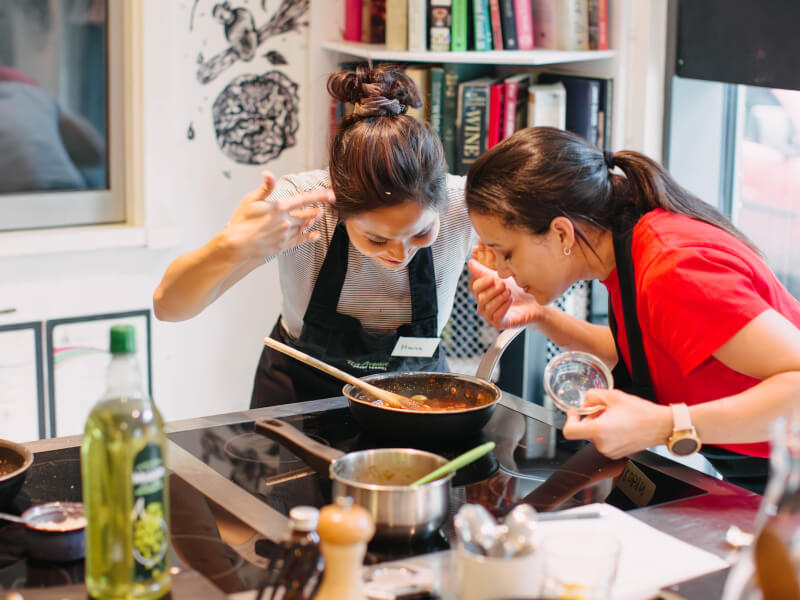 Two women enjoying a cooking class and smelling their food cooking with joy
